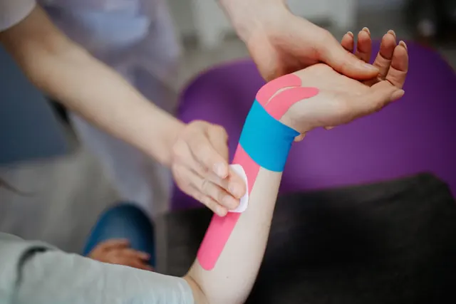 Terapeutti kiinnittää värillistä kinesioteippiä käsivarteen tukemaan kyynärvartta